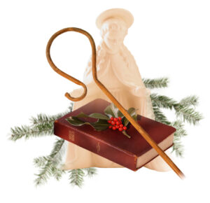 The image features a nativity scene with a beige-colored figure resembling a shepherd or saint, wearing a halo. In the foreground, there is an open wooden shepherd’s staff leaning across a red Holy Bible. The Bible is decorated with sprigs of holly and berries. Pine branches are also visible, suggesting a Christmas theme.