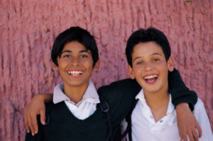 Two young boys smiling, with an arm around each other.